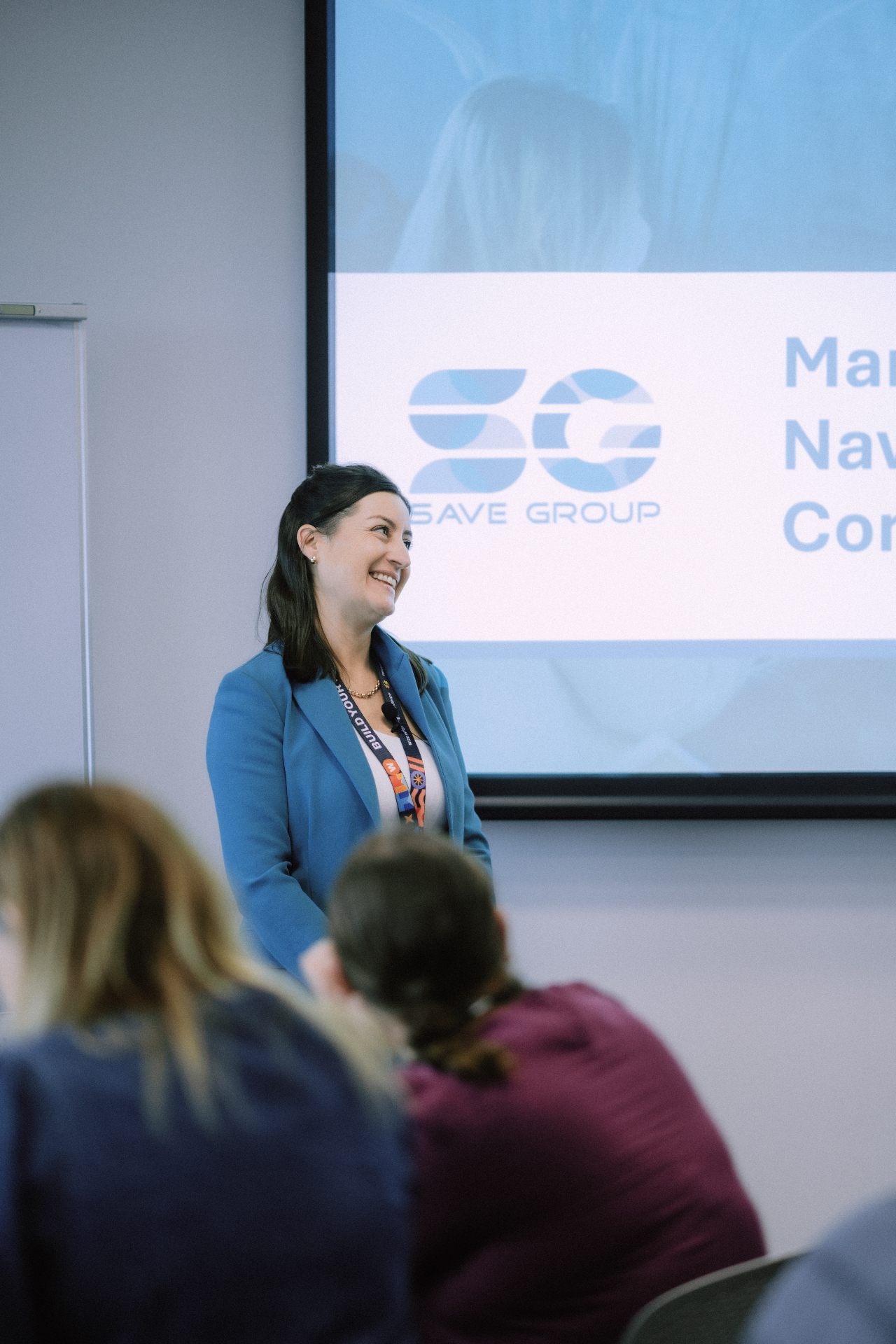Smiling presenter in a blue blazer beside a Save Group slide during the May 25 Day 1 workshop