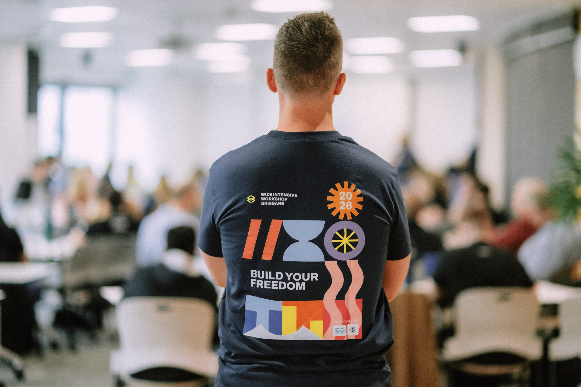 Wize team member standing in the workshop room wearing the Build Your Freedom Brisbane 2026 event shirt