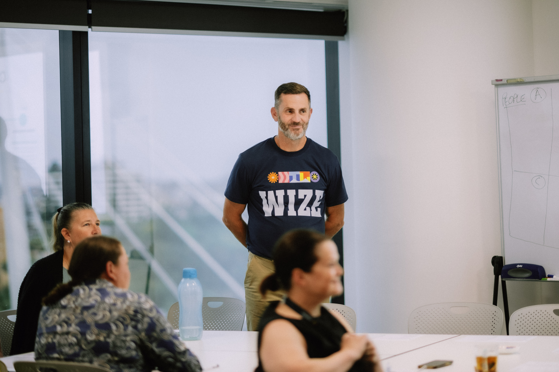 Facilitator in a Wize t-shirt smiling at the front of the workshop room