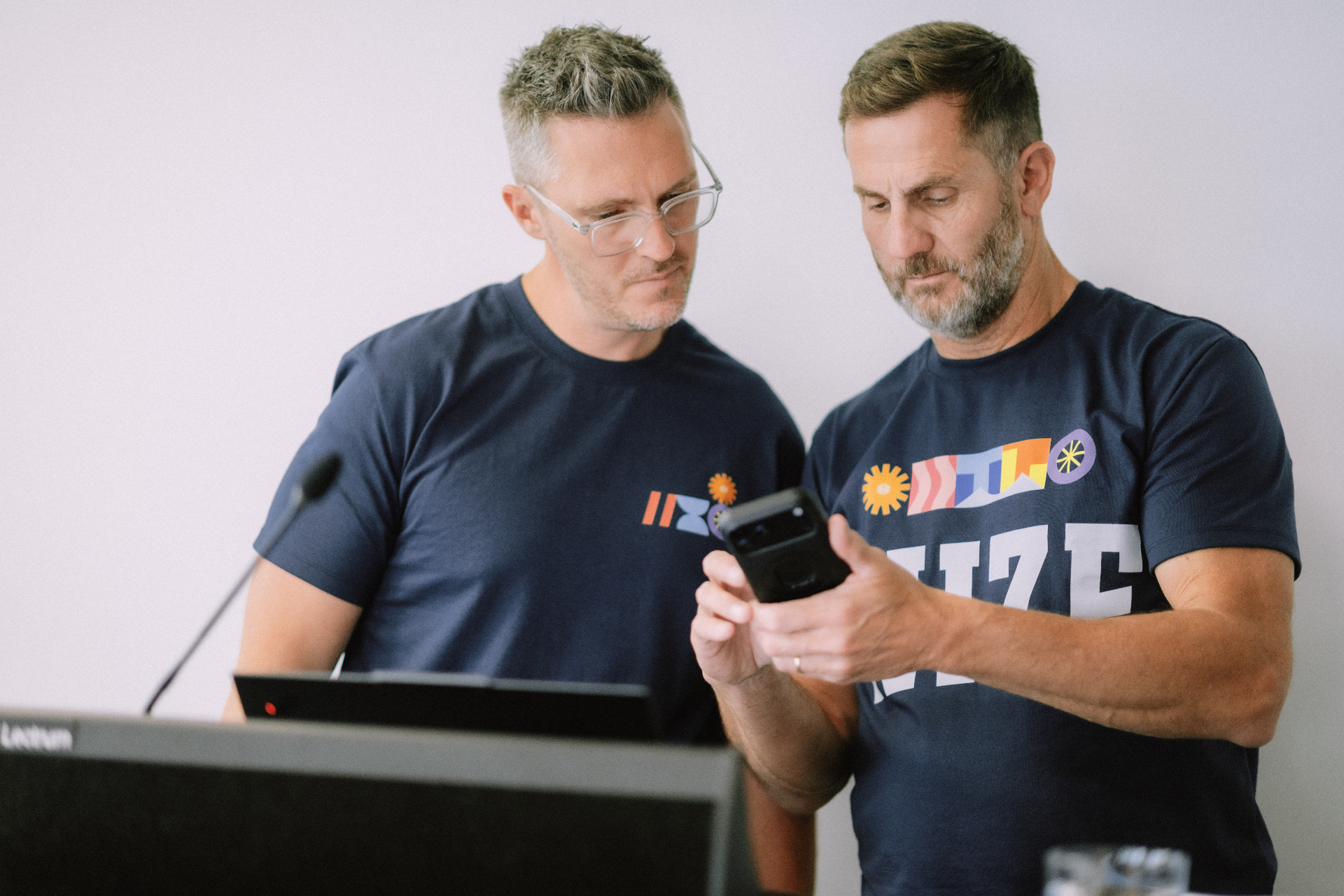 Two Wize coaches in branded shirts reviewing notes on a phone at the podium