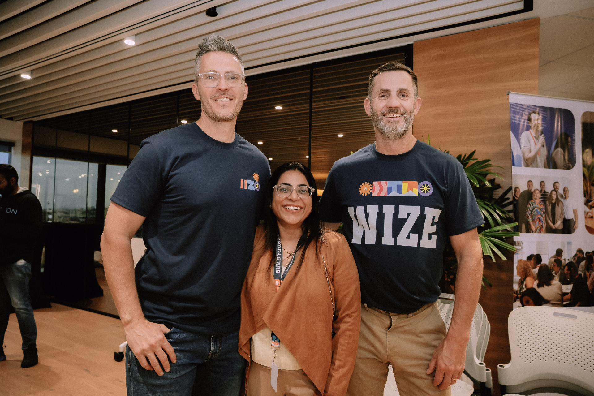 Two Wize team members posing with an attendee in front of the Wize banner