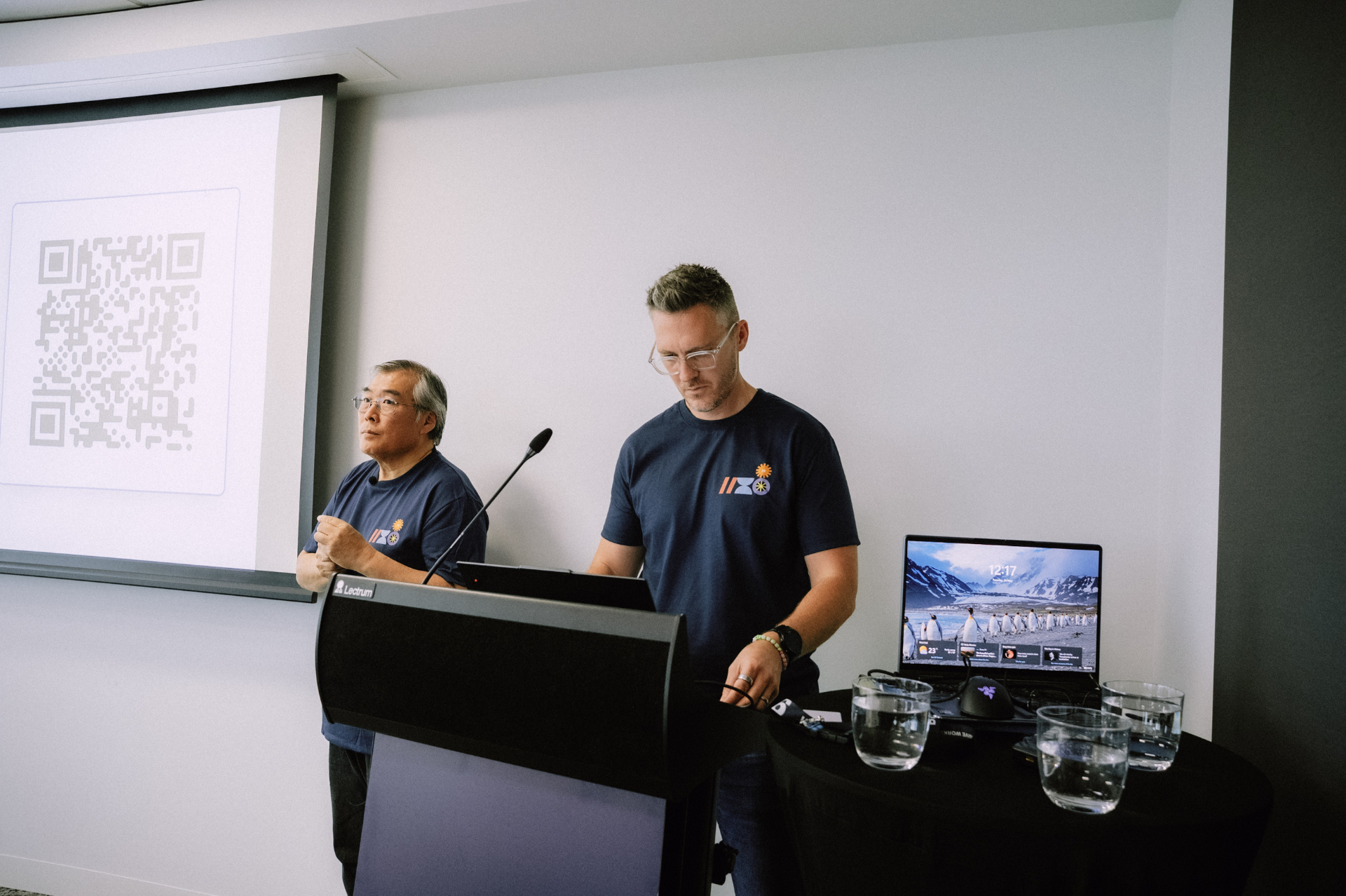 Two facilitators presenting from the lectern with a QR code on the projector screen