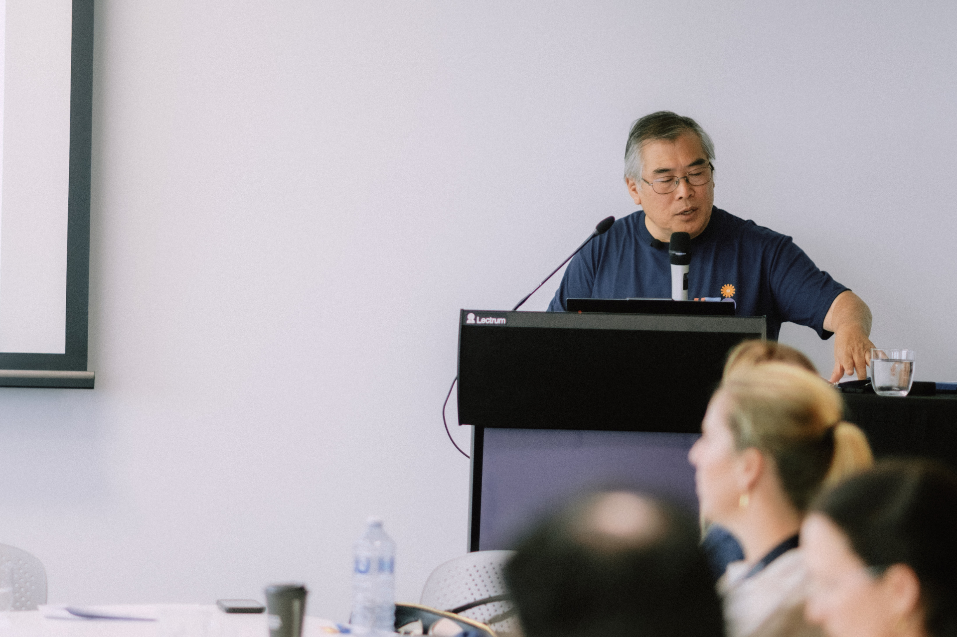 Guest speaker presenting from the lectern while attendees listen during the Day 4 workshop