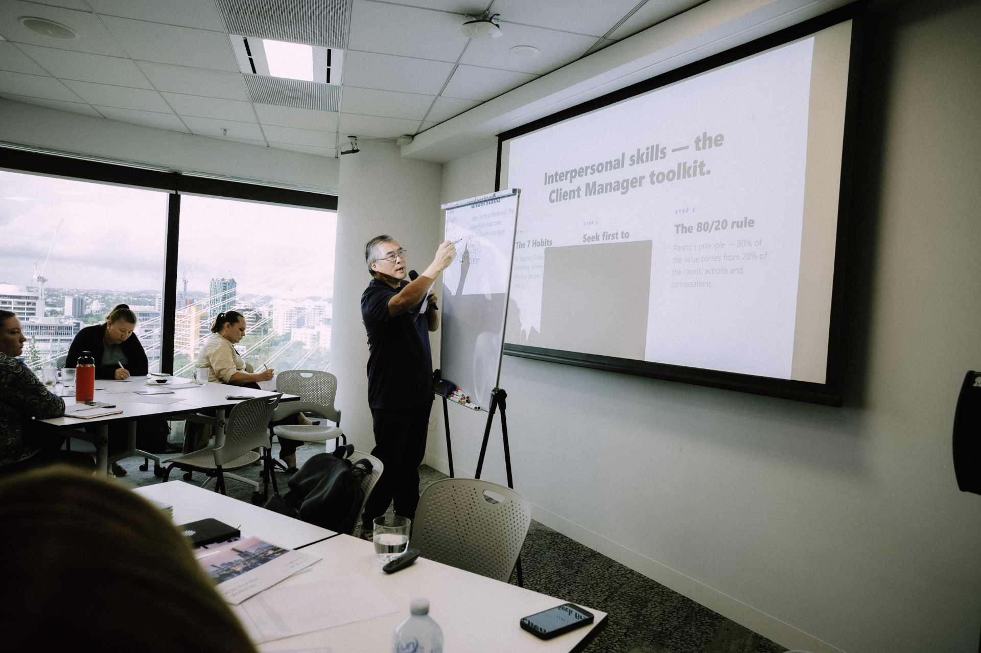 Facilitator presenting client manager toolkit concepts beside the projector screen