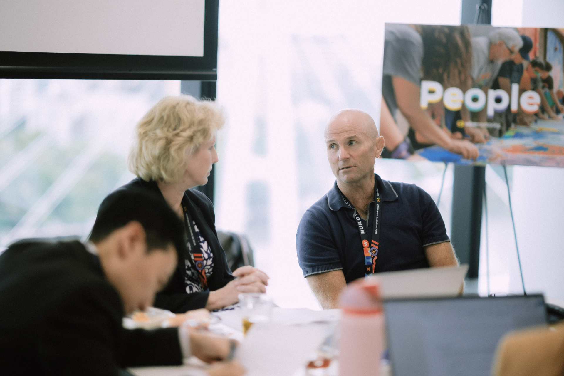 Attendees in close discussion at a table beside a 'People' display board