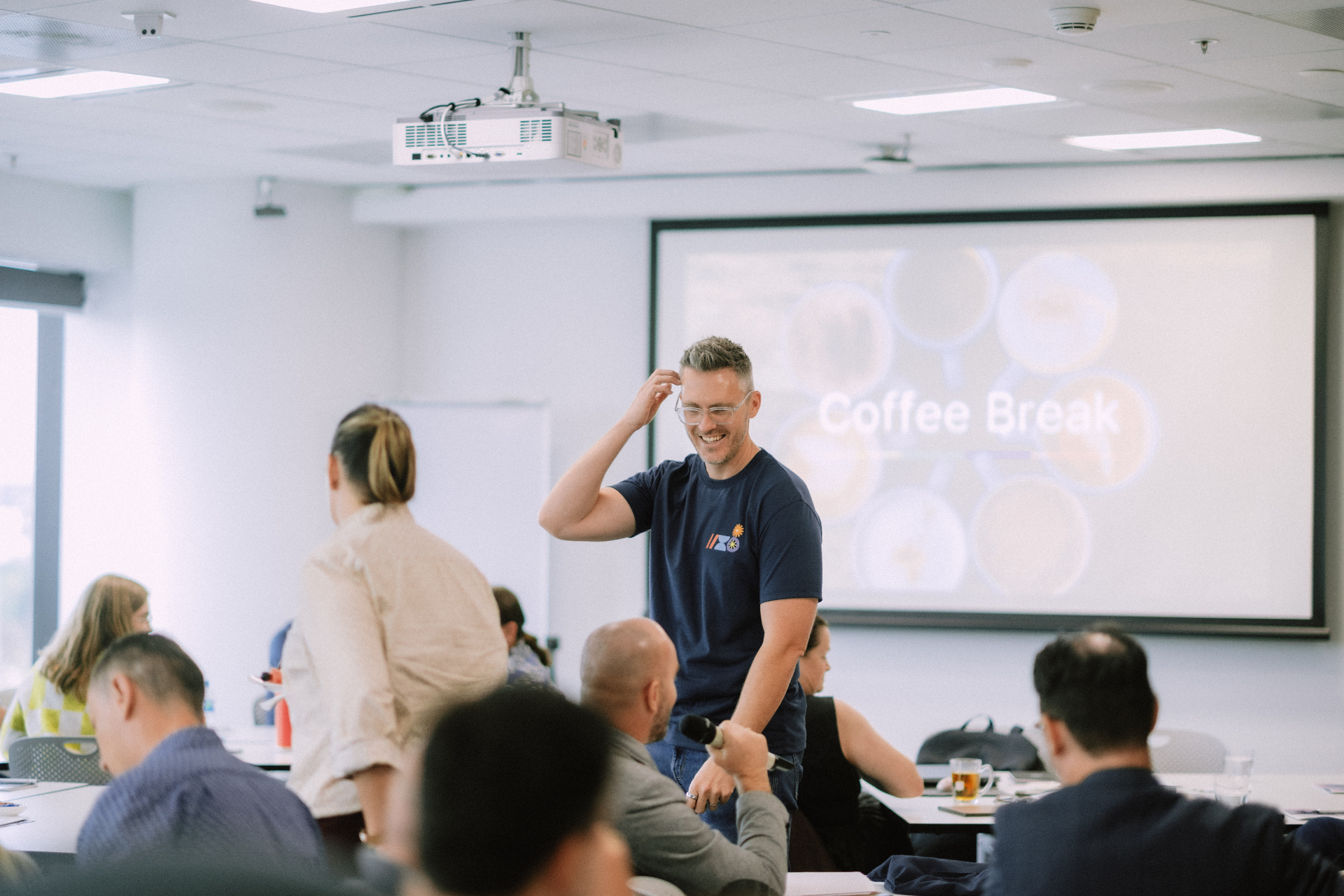 Facilitator laughing on stage with the Coffee Break slide projected behind